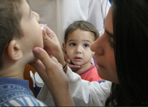AA young child receives the oral vaccine from WCMC-Q student Mahfam Shafaee as his friend looks over.